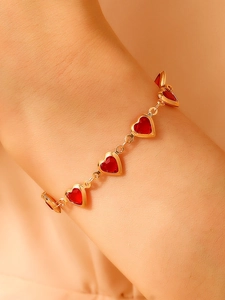 Gros plan d'un bracelet chaîne doré avec cinq pierres précieuses de cœur rouge au poignet