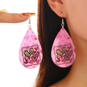 Detail of tear-drop earrings with pink heart patterns and silver hooks on model