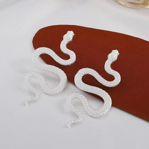Macro shot of silver snake earrings with textured scales on a red display card