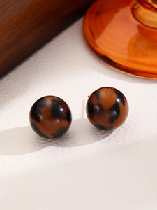 Macro detail of amber leopard print resin stud earrings on premium textured white leather