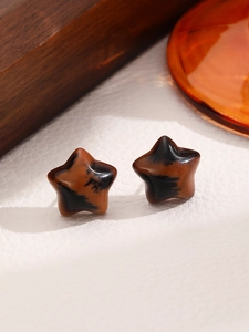 Macro shot of retro star-shaped tortoiseshell resin stud earrings on a textured background