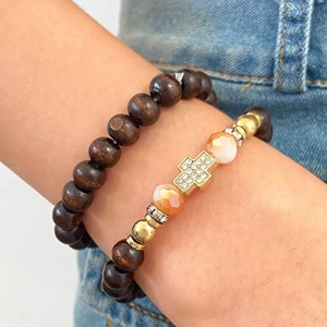 Detail of stacked bracelets featuring a sparkling cross pendant and dark wooden beads