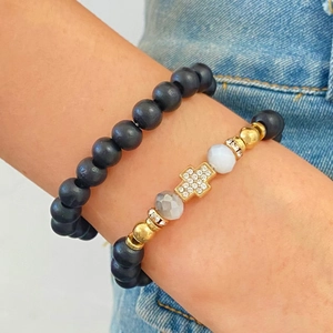 Detail of layered matte black beaded bracelets with a gold crystal cross charm for women