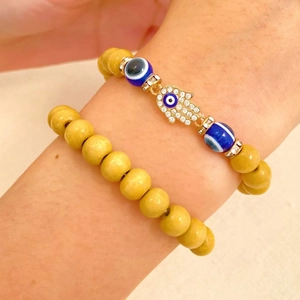 Close-up of stacked yellow beaded bracelets with Hamsa Hand pendant and Evil Eye charm