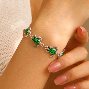 Dettaglio del bracciale con ciondolo a tartaruga e smalto verde sul polso donna