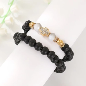 Detail of beaded bracelet set featuring a gold cross charm and black matte round beads