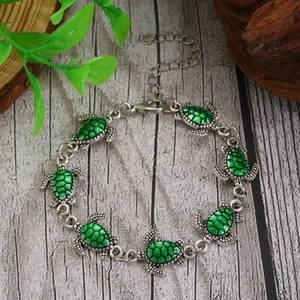 Bracciale a tartaruga in lega argentata con smalto verde su fondo in legno rustico