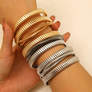 Detail of layered gold and silver Tubogas coil bracelets with elastic metal texture