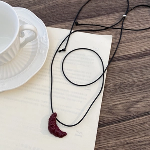Dettaglio della collana a forma di croissant su un tavolo di legno con una tazza