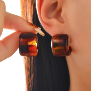 Macro shot of amber resin square hoop earrings with tortoiseshell texture on female ear