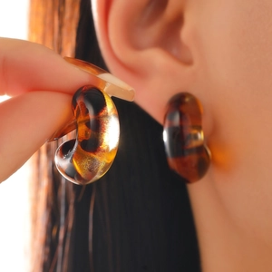 Close-up of amber tortoiseshell resin C-shaped stud earrings worn by a model