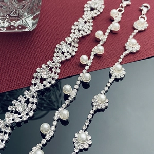 Detalle de pulseras tejidas de pedrería con perlas sobre una elegante superficie de espejo