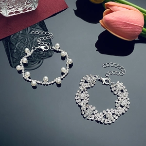 Detalle de pulseras de perlas y pedrería en forma de S sobre superficie reflectante negra