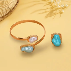 Detailansicht eines goldenen Armreifs mit Barockperlen und einem Ring mit Türkisstein