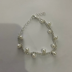 Detalle de pulsera de strass plateada con perlas blancas y cadena ondulada con cierre de langosta