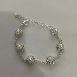 Detalle de pulsera plateada con pedrería trenzada, flores de perlas y cierre de langosta