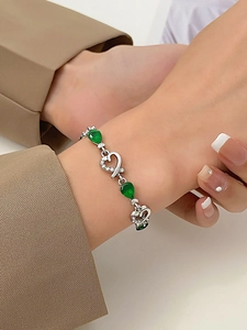 Detalle de la pulsera plateada con piedras verdes en forma de pera y adornos de corazón