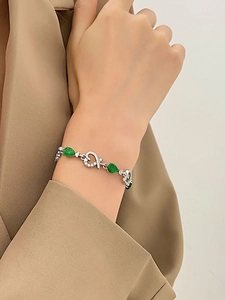 Detalle de una pulsera de plata con gemas verdes en forma de pera y detalles de corazón en la muñeca