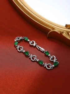 Detalle macro de la pulsera plateada con gotas color esmeralda y cristales en forma de corazón