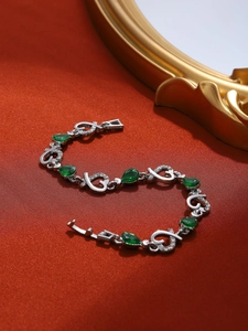 Detalle de pulsera de plata en forma de corazón con piedras verdes sobre seda roja