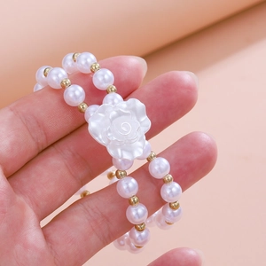 Detail view of a double-layer pearl bracelet featuring a white rose flower charm on a hand