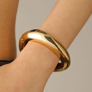 Polished thick gold geometric spring open bangle showing reflective mirror metal finish