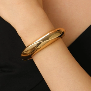 Close-up of minimalist polished gold wide cuff bracelet on wrist with mirror-like finish