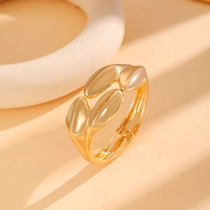 Close-up of golden geometric spring bangle with leaf-shaped accents on minimalist stand