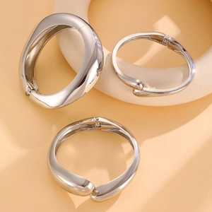 Detailed view of three silver alloy spring hinge bracelets on minimalist beige background