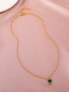 Detailaufnahme der goldenen Halskette mit grünem Herz-Anhänger auf rosa Seide