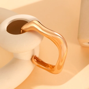 Detailed view of wide gold geometric bangle with high-gloss mirror finish on ceramic