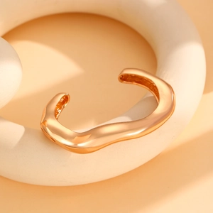 Detail of wide golden open bangle with irregular wavy texture and mirrored finish