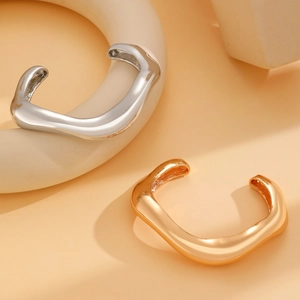 Detailed view of glossy gold and silver liquid metal bangles on minimalist pedestals
