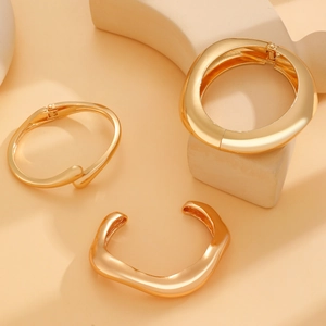 Detailed close-up of three polished gold alloy bangles with wide and irregular shapes