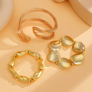 Detailed view of polished gold geometric cuff and spring bracelets on apricot background