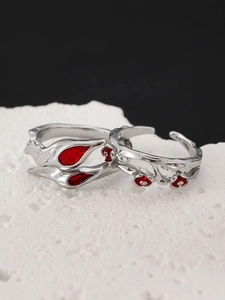 Macro shot of silver-colored flower rings with red enamel details on a white rock base