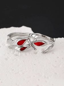 Macro detail of silver branch rings with red leaf accents on white stone surface