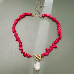Detail view of deep red stone necklace with gold toggle clasp and baroque pearl charm