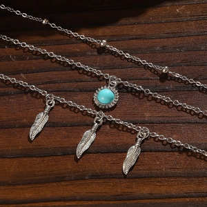 Detail view of multi-layer silver necklace with metal feathers and turquoise bead on wood