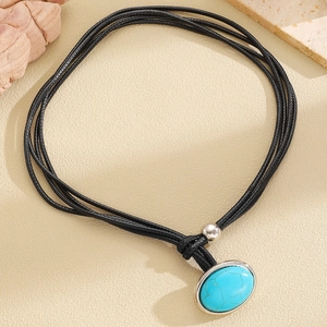 Detail view of oval turquoise pendant with silver frame on black woven cord necklace