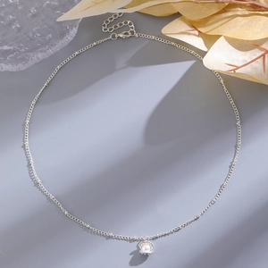 Detail of silver shell necklace with a pearl pendant on a soft textured background
