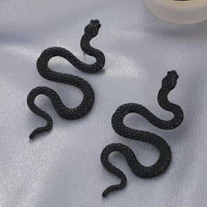 Close-up of matte black snake-shaped earrings with detailed scale texture on silk fabric