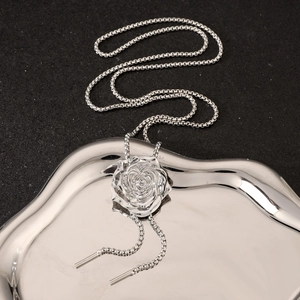 Detail of silver rose pendant on bolo tie style chain over a metallic tray background