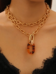 Close-up of layered gold chunky chain necklace with brown marble pendant and toggle clasp