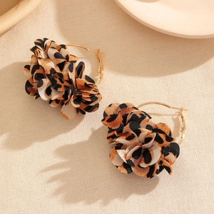 Detailed view of leopard print fabric flower earrings with golden hoops on beige fabric