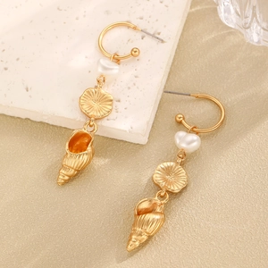 Detailed close-up of gold conch shell earrings with heart pearl and sunburst charms