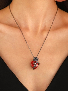 Close-up of gothic necklace with a red heart gem and black metal rose on skin