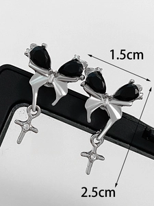 Macro detail of silver bow earrings with black gems and cross pendant showing 1.5x2.5cm size