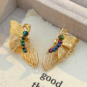 Close-up of golden butterfly earrings with iridescent beads and hollow floral details