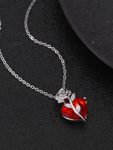 Close-up of red heart crystal pendant wrapped in silver rose branch on a fine chain